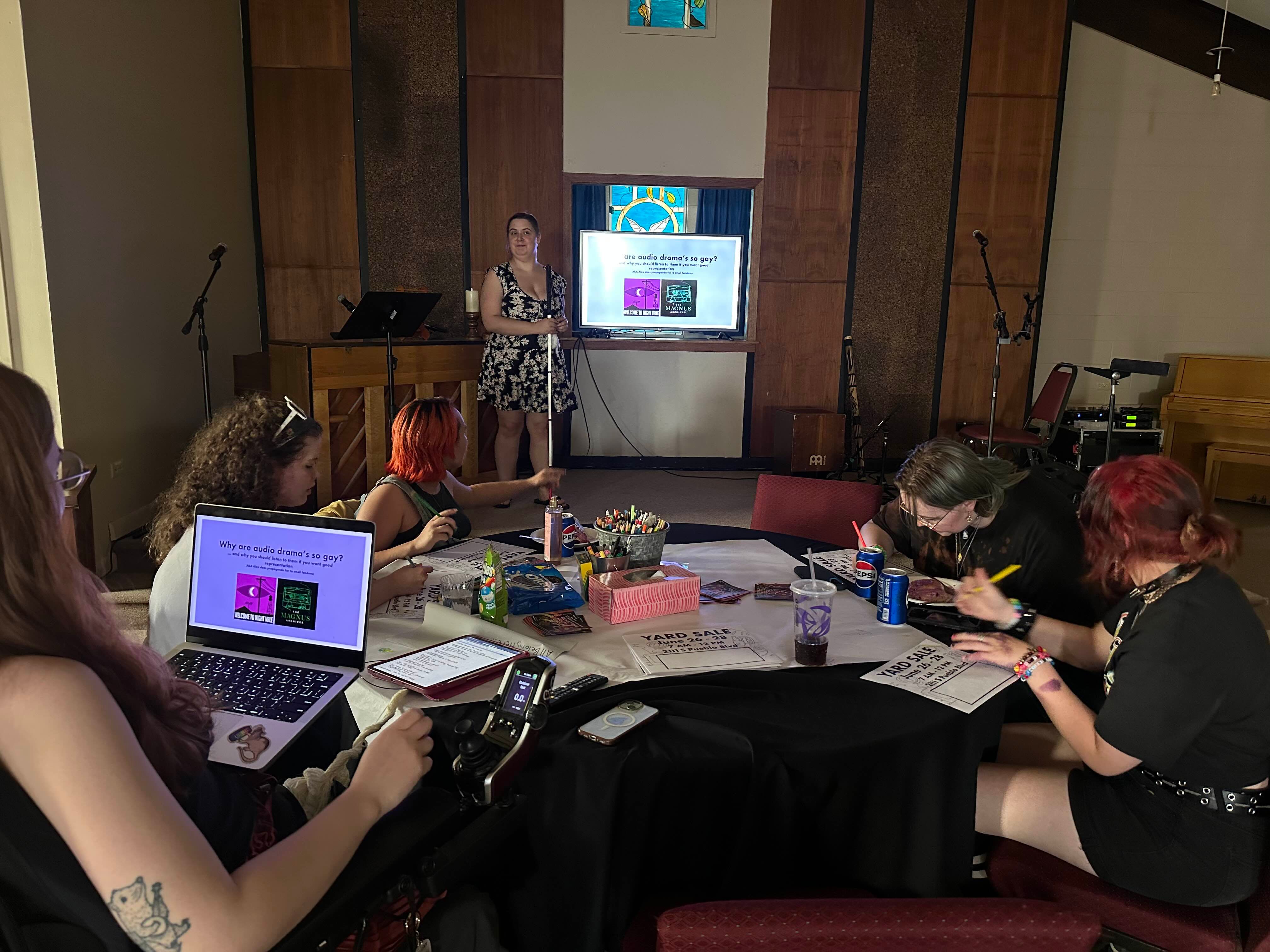various people sitting around a table working on art projects listening to another person present a slideshow of information